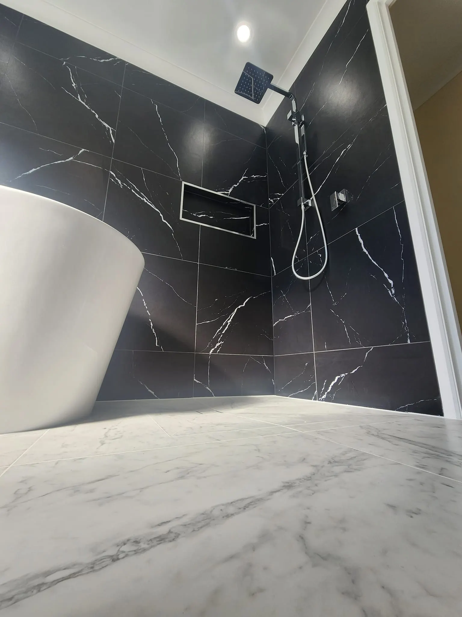 Completed bathroom in black marble tile with freestanding bath and wall-mounted mixer